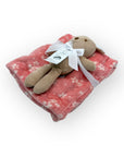 Stuffed animal toy on a pink floral blanket with a white ribbon on a white background