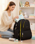 Stork And Baby black linen diaper backpack with yellow accents, organized for baby essentials. A woman is packing a blanket.