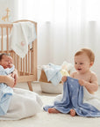 Stork And Baby blue bamboo blend hooded towels with white cloud and snowflake prints. A mother holds a newborn wrapped in one towel, while a toddler plays with another.