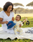 Stork And Baby blue denim bucket hat with red "SPORT" embroidery, for babies. A mother holds it for her smiling baby.