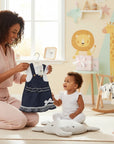 Stork And Baby denim pinafore and t-shirt set for infant girls, featuring a dark wash denim pinafore with a bow and ruffled hem, paired with a white t-shirt.