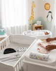 Stork And Baby black beanie with white stars, white beanie with mountain print, and baby booties on a grey blanket in a crib.
