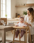 Stork And Baby Girls 3 Piece Set 18M: baby in floral top and mauve pants in high chair, with mother beside her.