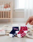 Stork And Baby girls' 2-pack non-slip socks in navy with floral embroidery and pink with floral print. White ruffled cuffs and non-slip grips.