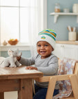 Stork And Baby white knit infant hat with green, blue, and orange stripes and a truck applique. A smiling baby wears the hat.