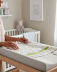 Stork And Baby white infants cutwork blanket with fairytale print and green trim. A woman is folding it on a changing table.