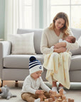 Stork And Baby Infants winter hat with navy and white stripes, navy pom-pom, and embroidered anchor detail.