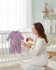 Stork And Baby lavender velour baby grower with giraffe print and "Long Hug" text. A mother holds her baby next to it.