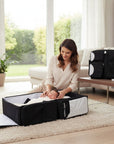 Stork And Baby Mothers Choice 3-in-1 travel bag unfolded as a portable baby bed with a sleeping infant in a living room