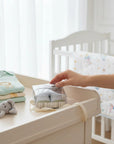 Stork And Baby olive and grey patterned baby socks in a gift box, with a stack of baby onesies and a rattle nearby.