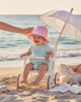 Stork And Baby pink anglaise hat with white trim on a smiling baby sitting in a stroller on the beach.