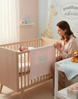 Stork And Baby pink cotton waffle blanket with embroidered heart and "dream" text. Baby in crib.