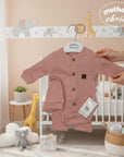 Stork And Baby pink ribbed 3-piece newborn set with bodysuit, hat, and pants. Features wooden buttons and a cute patch.