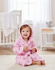 Stork And Baby pink 100% polyester baby bathrobe with tiara print and hood. A smiling toddler sits on a rug.