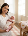 Stork And Baby mother holding a newborn baby girl in a rainbow print sleep sack and pink hat. Nursery setting.