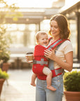 Stork And Baby red 6-way baby carrier with adjustable straps and padded support, worn by a smiling mother holding coffee.