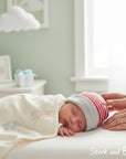 Stork and Baby striped knit baby hat with red and grey bands, worn by a sleeping infant.