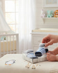 Stork And Baby blue and white striped baby socks in a clear box, with a baby's foot reaching for them. Cotton blend.