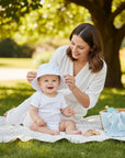 Stork And Baby white 100% cotton woven sun hat with flower detail for baby, worn by a smiling baby outdoors.