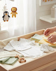 Stork And Baby white textured romper and bib with polka dot booties and soft blankets on a changing table.