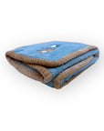 Folded blue blanket with brown trim on a white background