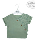 Green baby wrap top with dinosaur print on a hanger against a white background