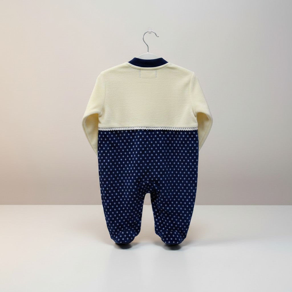 Baby outfit with cream top and navy polka dot pants on a hanger against a light background