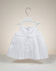 White pleated dress on a hanger against a beige background