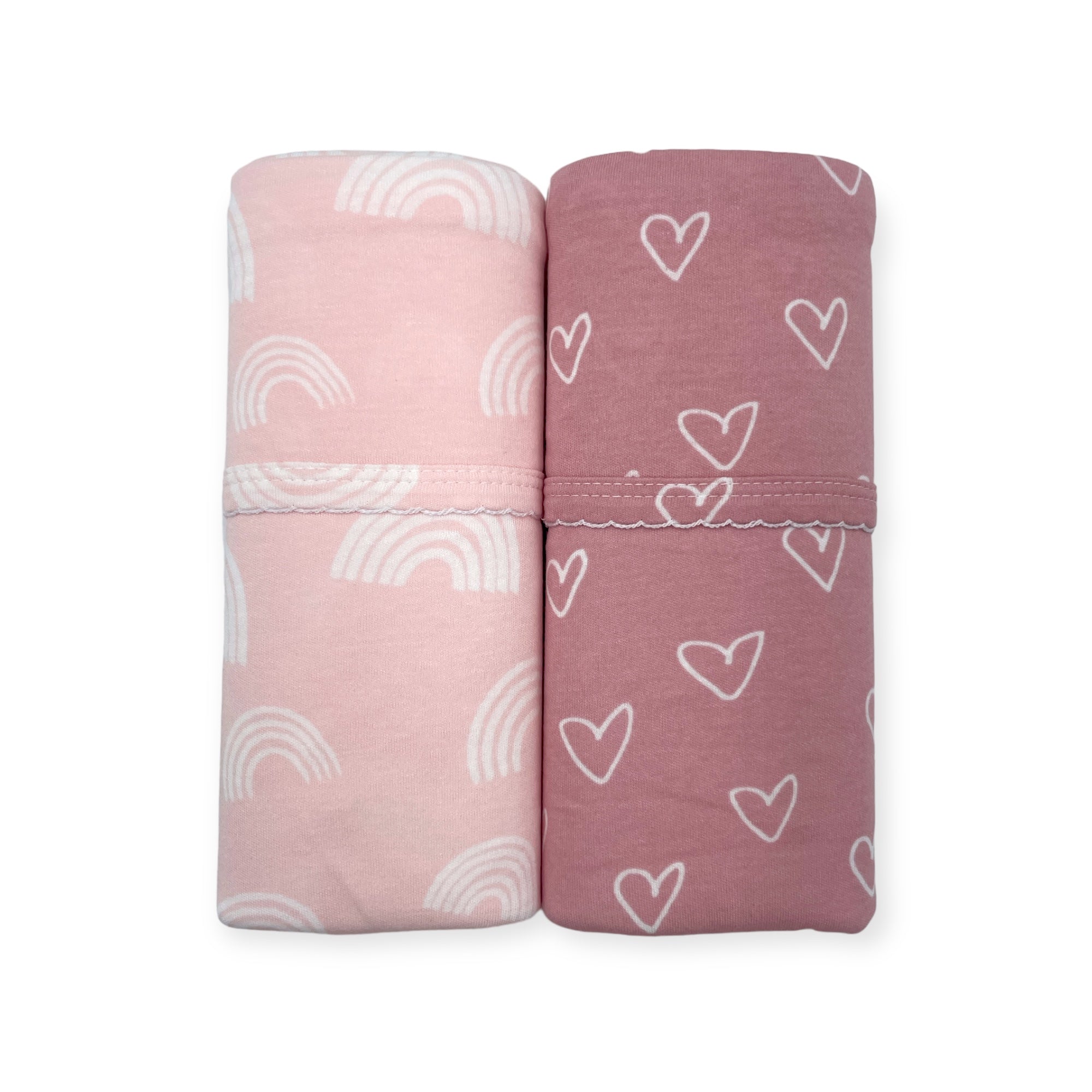 Two folded fabric swaddles with rainbow and heart patterns on a white background