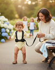 Stork And Baby black baby walking harness with elephant detail, worn by a toddler outdoors with a woman holding the leash.