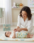 Stork And Baby boys romper with a playful zoo print, white top, and green/orange bottoms. A mother is dressing the baby.