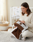 Stork And Baby brown sherpa fleece baby blanket with white trim, featuring corduroy texture. A woman holds it near a crib.