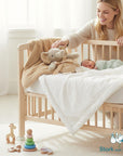 Stork And Baby soft tan plush elephant toy with ribbon and a beige fuzzy blanket in a crib with a newborn baby.