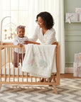 Stork And Baby Girls 3 Piece Set: baby in floral top and mauve pants, with a woman in a white shirt in a crib.