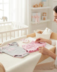 Stork And Baby Girls Dino 3-piece set: grey bodysuit with pink trim, pink floral print shorts with ruffles, and matching socks.