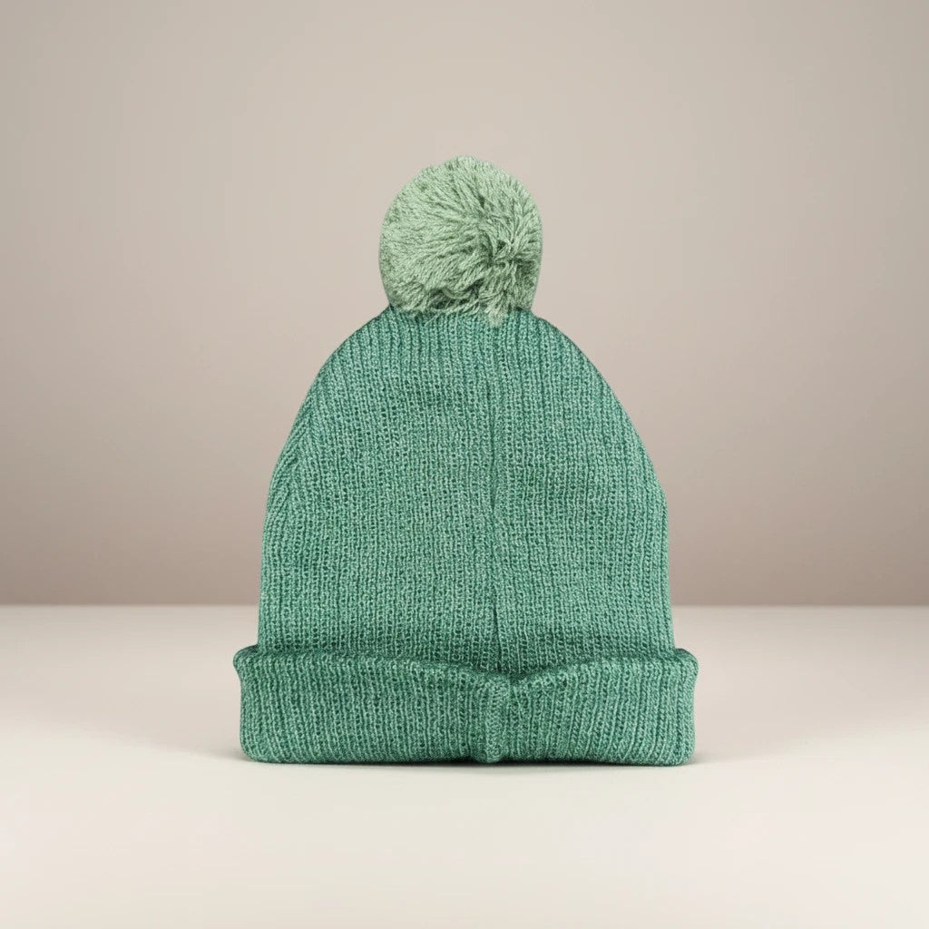 Stork And Baby green knit pom pom beanie for babies, perfect for winter outings and cozy cuddles.