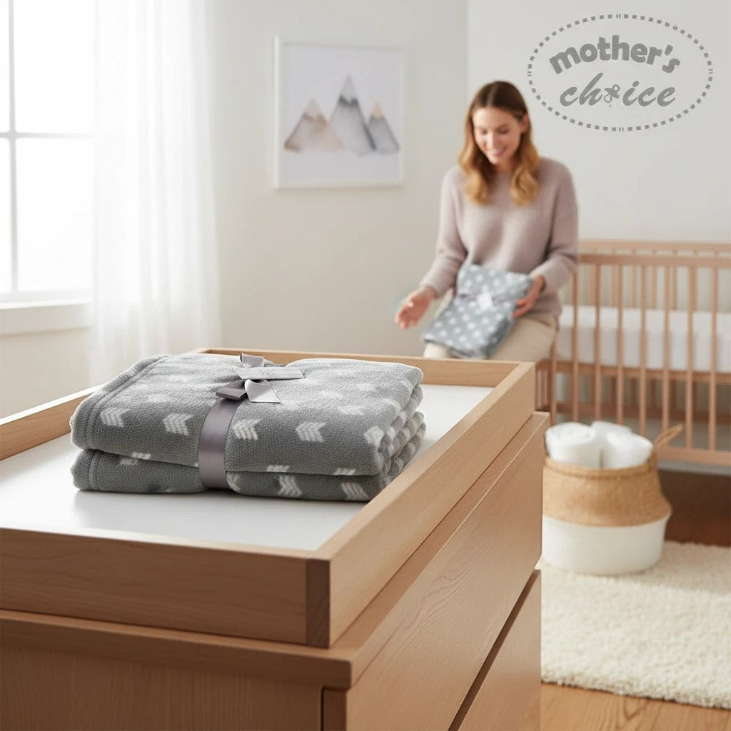 Stork And Baby Mother's Choice grey fleece baby receiver blanket with white arrow pattern, folded on a wooden dresser.