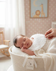 Stork And Baby white embroidered linen/cotton bib with floral accents on sleeping infant.