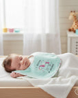 Stork And Baby infant's light blue bib with a pink unicorn graphic and 'I Believe In Unicorns' text.