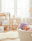 Stork And Baby purple and pink striped infants winter hat on sleeping baby in a basket
