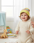 Stork And Baby yellow striped knit infants winter hat on a smiling baby wearing a cream romper.
