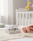 Stork And Baby leopard print infant socks in a clear box, with baby feet nearby.