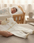Stork And Baby cream longsleeve footed baby grower with a basket detail and beige trim. A baby sleeps in the background.