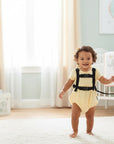 Stork And Baby Mothers Choice 2 In 1 Bee Harness on a smiling baby in a yellow romper, with a mother holding the leash.
