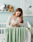 Stork And Baby Mothers Choice sage green bamboo cotton muslin wrap with white leaf print. Woman holding baby.