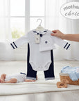Stork And Baby white long-sleeve romper with navy sailor collar and trim, navy pants, and matching hat. A baby lies on a rug.