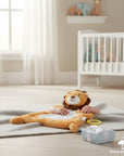 Stork And Baby Mothers Choice Nunu Blanket Lion plush toy with a baby's hands resting on it, on a grey blanket.