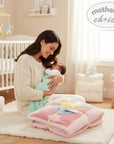 Stork And Baby pink cutwork blanket with pastel squares and yellow ribbon, held by a mother with her newborn baby.