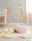 Stork And Baby pink heart-shaped baby pillow with "baby" embroidered, next to a sleeping infant on a yellow blanket.