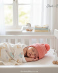 Stork and Baby pink knitted pom pom beanie on a sleeping baby in a crib